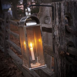 A glass lantern hanging on a fence with a lit candle inside