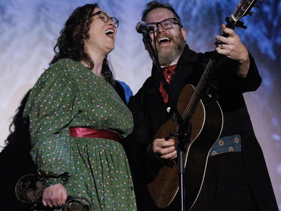 A man and woman sing joyfully while a man plays guitar