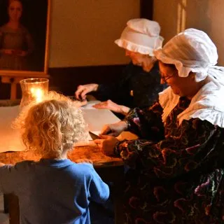 A young child gets a card stamped by a person dressed in 1830s attire