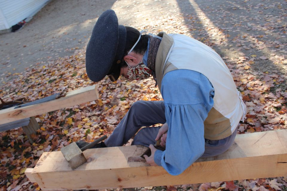 A costumed historian cutting a mortise