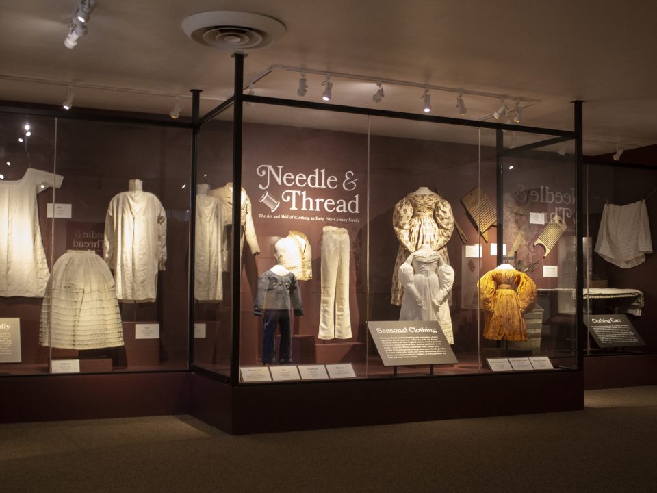 A variety of 1830s garments including gowns, petticoats, tailcoats, and more on display