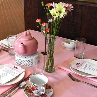 A table set with flowers, tea cups and saucers, silverware and a pink teapot