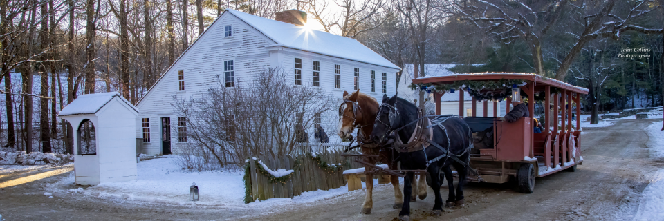 A horse drawn carryall drives by a white house in winter