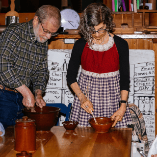 Two adults stir food in redware pottery bowls